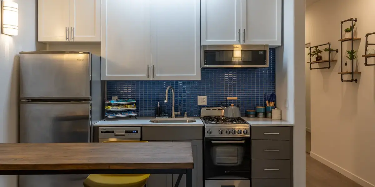 A modern kitchen featuring white cabinets, a stainless steel refrigerator, a stove, and a dining table with yellow stools.