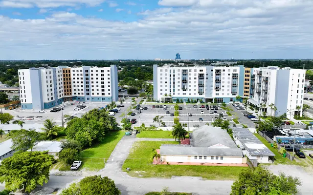 An aerial view of a modern apartment complex with several buildings and parking lots, surrounded by greenery.