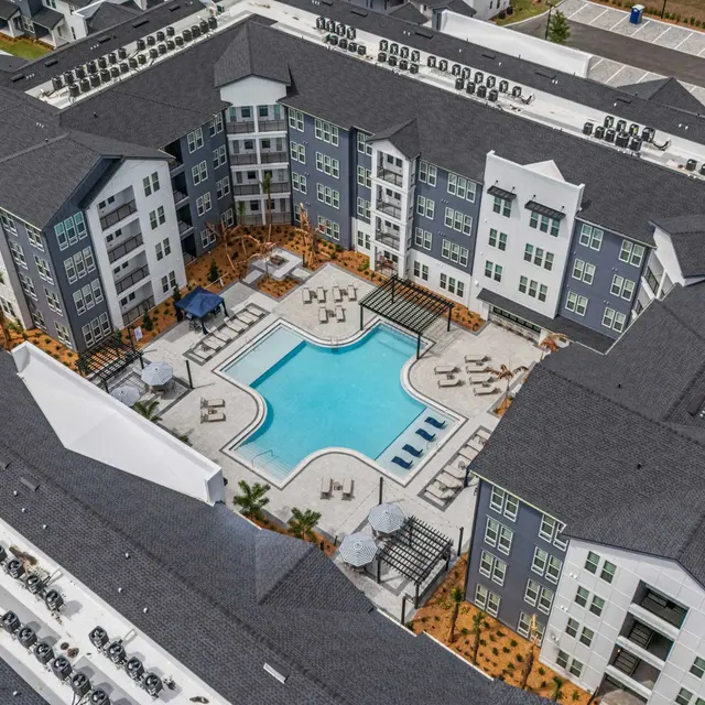 Modern Apartment Complex with Pool Aerial view of a modern apartment complex featuring multiple buildings surrounding a central swimming pool and lounge area.