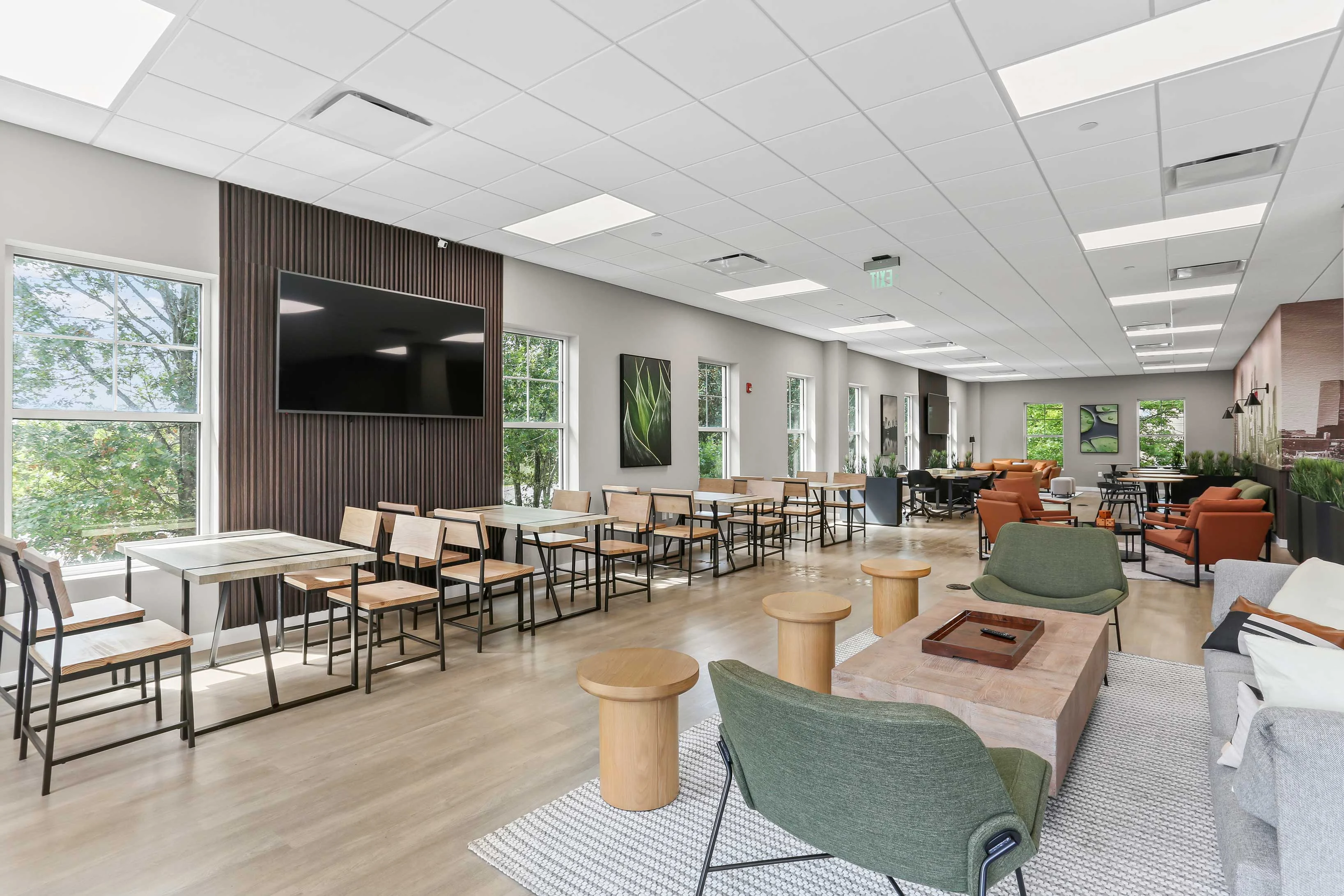 Modern Lounge Space A spacious modern lounge area featuring large windows, a flat-screen TV on the wall, and various seating arrangements including tables and chairs, a sofa, and armchairs.