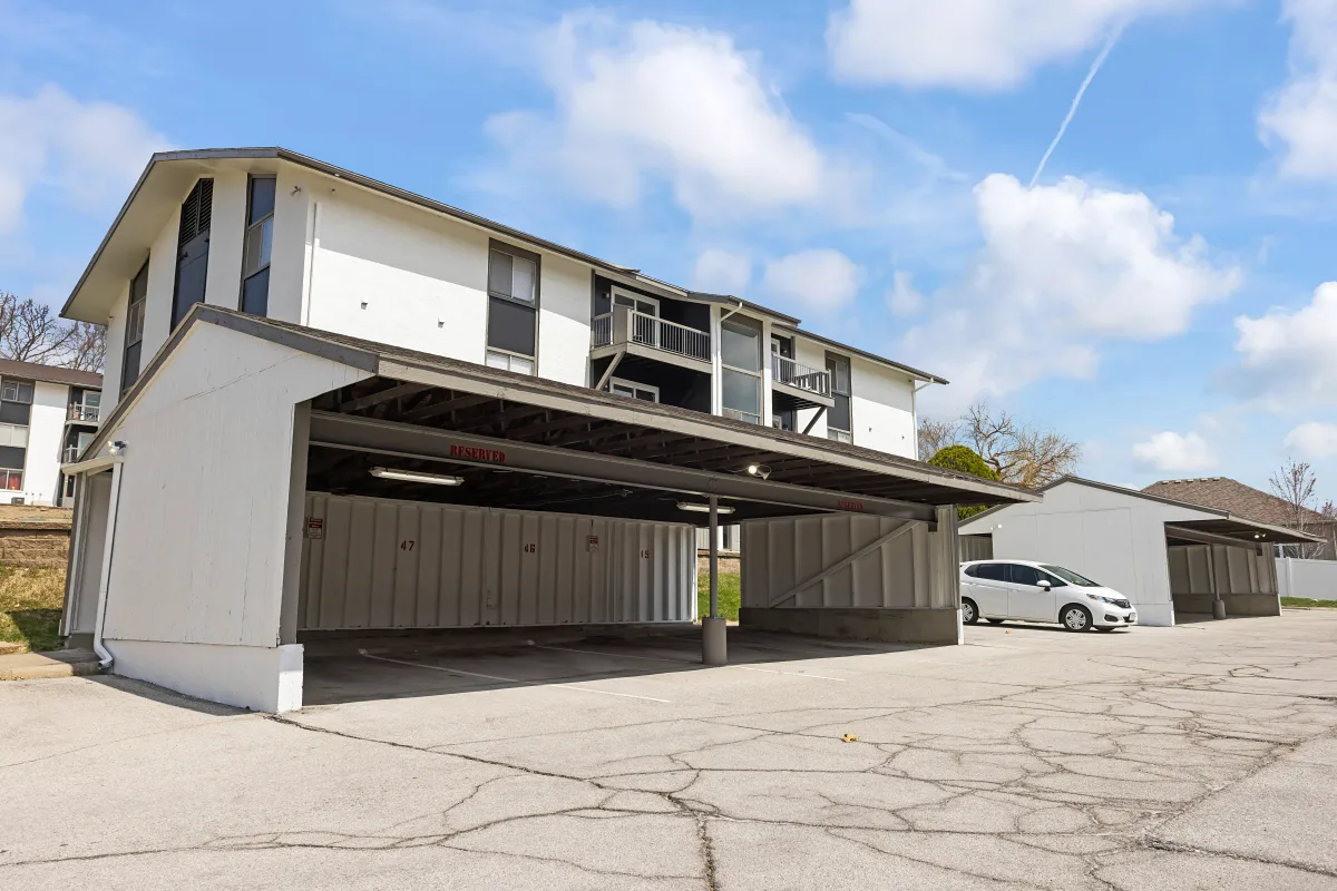 Apartment Parking Structure A view of a parking structure with covered spaces in front of an apartment building, featuring a white car parked in one of the spaces on a clear day.