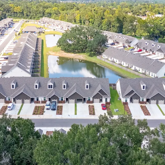 Aerial View of a Residential Community Aerial view of a modern residential complex featuring multiple buildings, a pond, and shaded green areas.