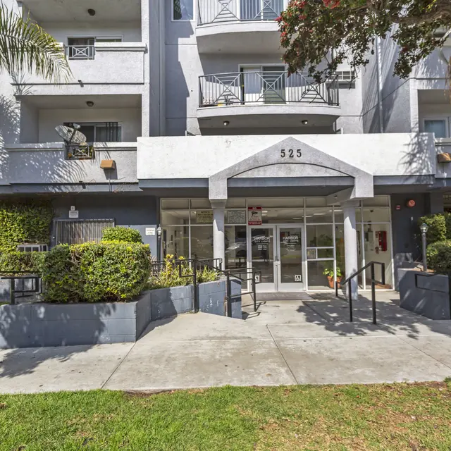 The entrance of a multi-story building featuring a glass door and surrounding greenery.