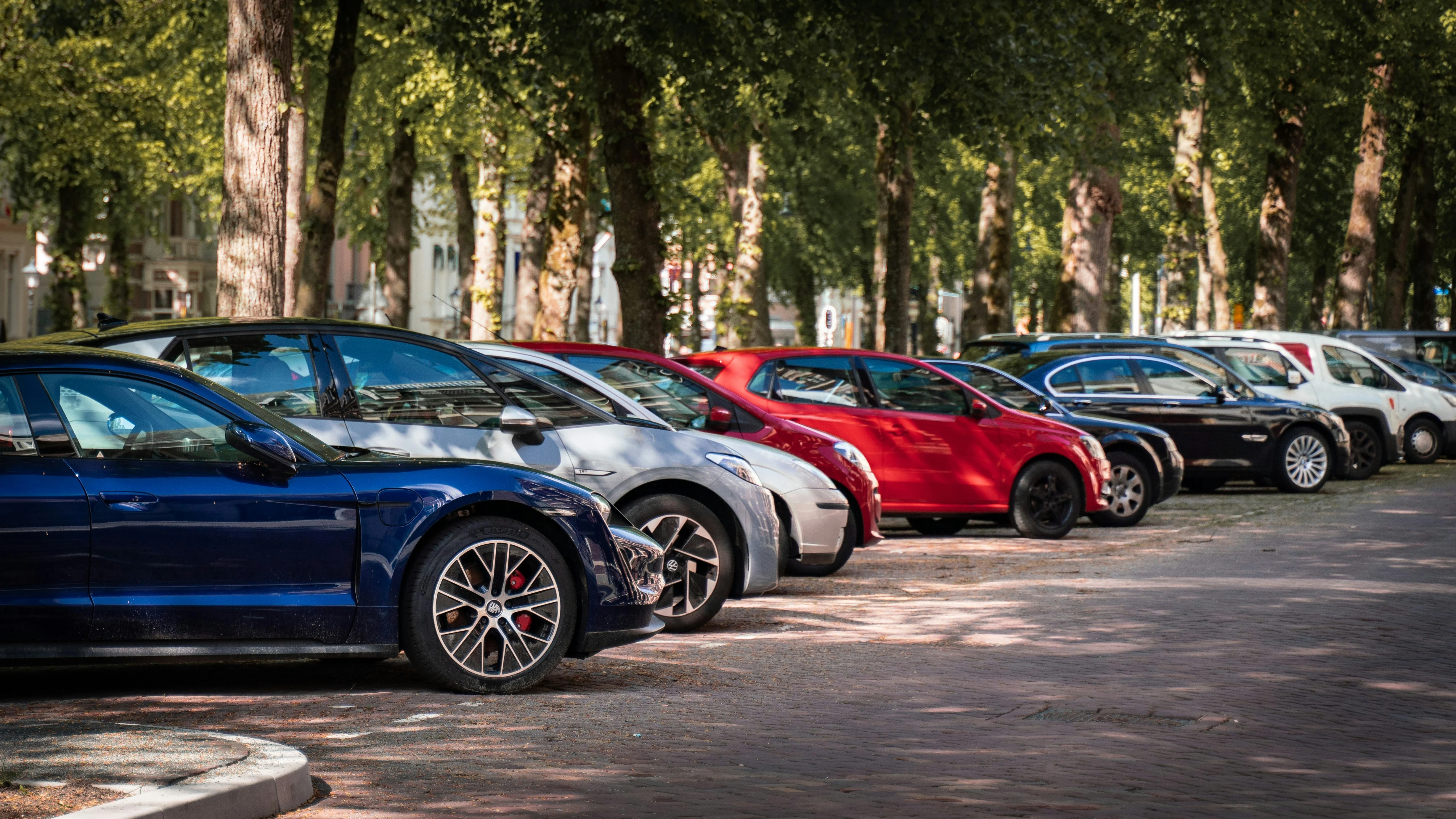 Row of parked cars in a tree-lined street during daytime.
