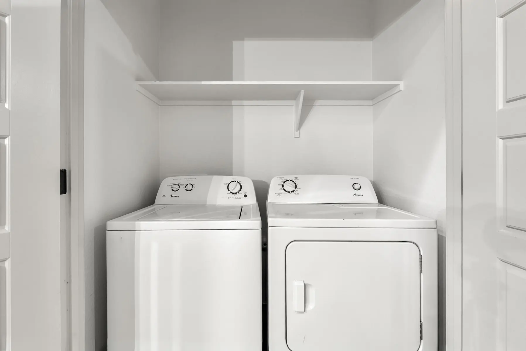 A laundry room featuring a white washing machine and dryer side by side, with a shelf above in a well-lit space.
