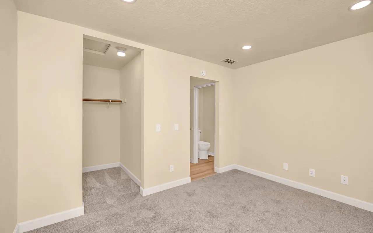 An empty bedroom featuring beige walls, carpeted flooring, a small closet on one side, and a door leading to a bathroom.