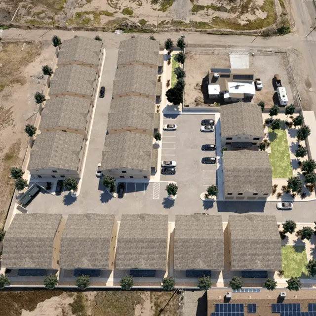 Aerial view of a housing development featuring multiple residential buildings, parking areas, and green spaces.