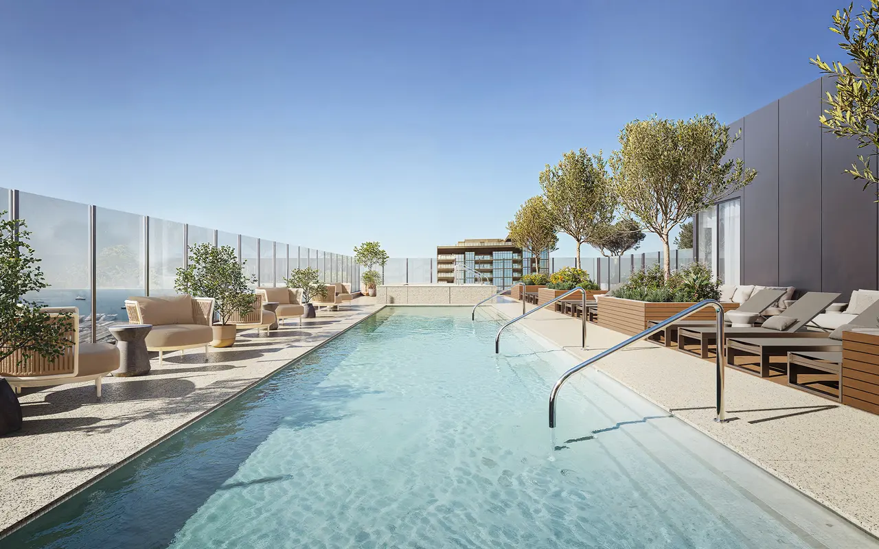 A modern rooftop pool area with a clear sky. The pool features stainless steel handrails, lounge chairs, and potted trees around the perimeter.