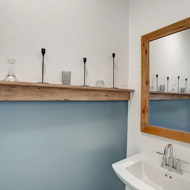 Modern Bathroom Decor A contemporary bathroom featuring a wooden shelf with various glass items and candles, a large wall mirror, and a modern sink.