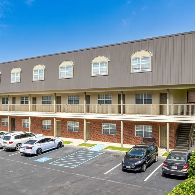 Exterior view of a multi-story apartment building with balconies and a parking lot.