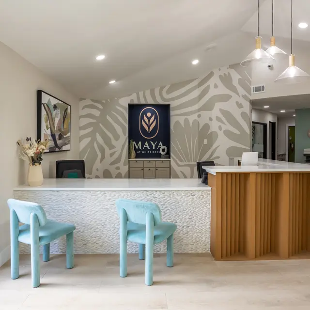 A modern reception area featuring a white stone desk with a wooden front, decorative wall art, and two light blue chairs.