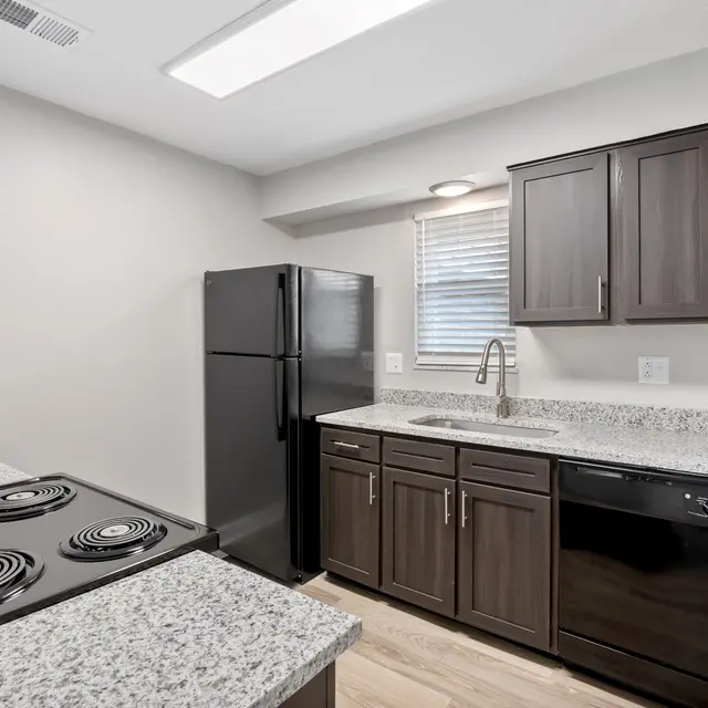 Modern kitchen featuring black appliances, dark wood cabinets, granite countertops, and natural light from a window.