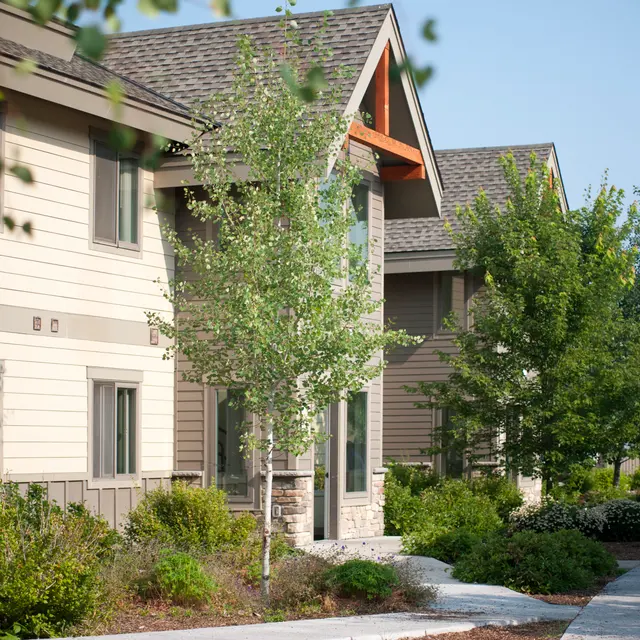Residential Area in Nature A row of residential buildings featuring a combination of wood and stone exteriors, surrounded by green trees and shrubs in a landscaped area.