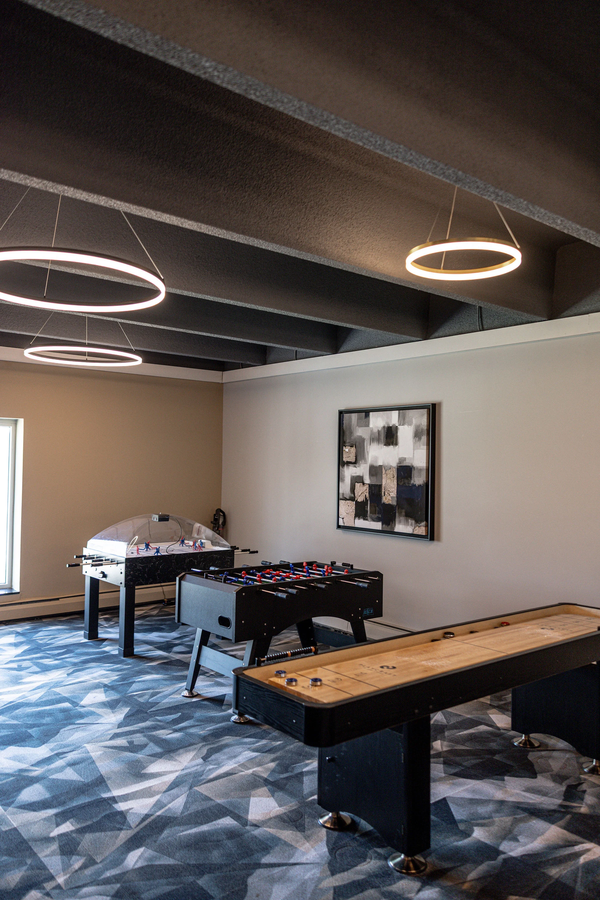 Community Gaming Area A recreational gaming area featuring a shuffleboard table, a foosball table, and a large dome-shaped air hockey table. The space has modern lighting fixtures and a patterned carpet.