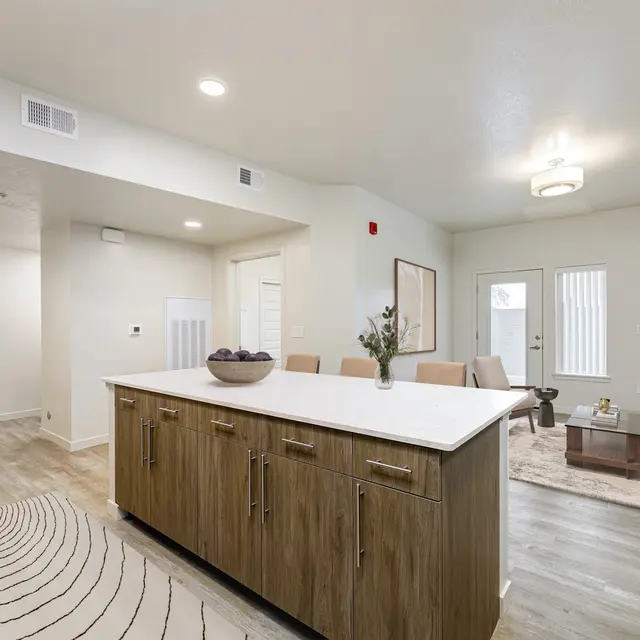 A modern open concept living area with a kitchen island, dining table, and living room furniture in neutral colors.