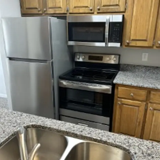 A modern kitchen featuring stainless steel appliances including a refrigerator, microwave, and oven, with wooden cabinetry and a granite countertop.