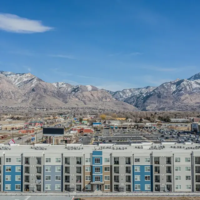 Aerial view of a modern apartment complex with a mountain backdrop, showing various rooftops and the surrounding landscape.