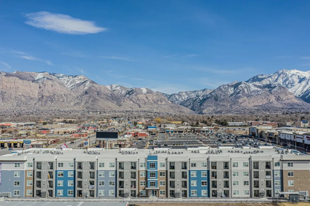 Aerial view of a modern apartment complex with a mountain backdrop, showing various rooftops and the surrounding landscape.