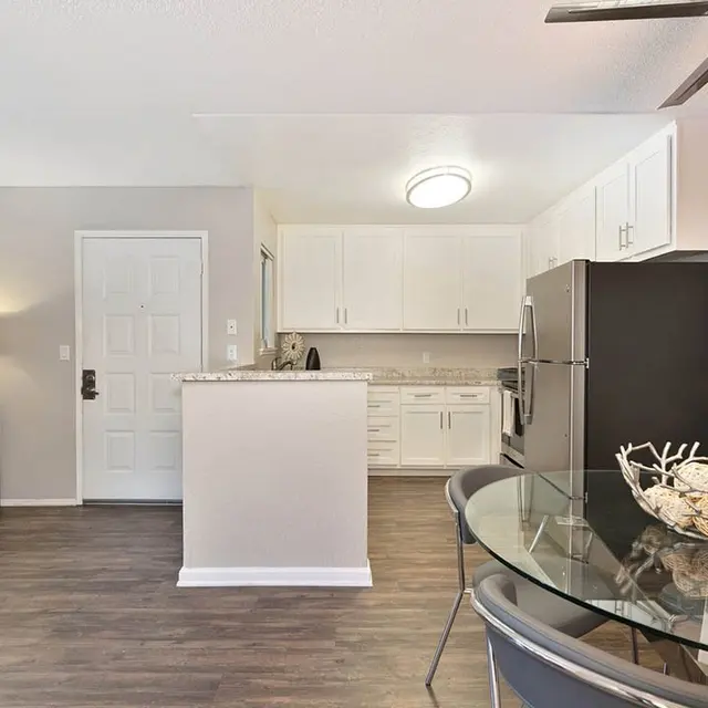 A modern kitchen area featuring white cabinetry, stainless steel appliances, and a dining table with a decorative centerpiece.