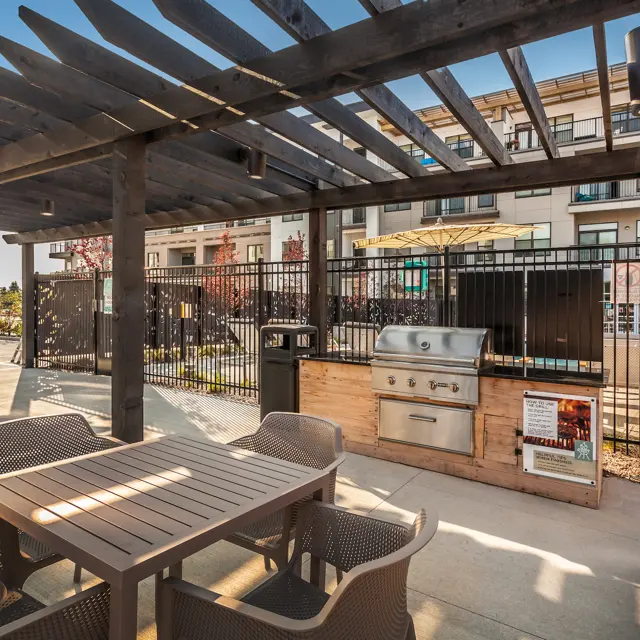 An outdoor grilling area with a gas grill and dining tables under a wooden pergola.
