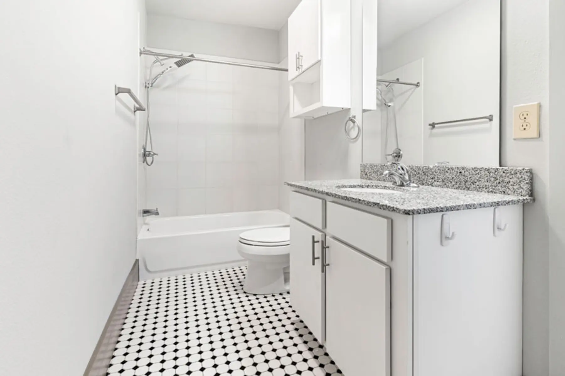 A modern bathroom with a bathtub, shower area, and vanity sink featuring white cabinets and a granite countertop. The floor has a black and white checkered pattern.