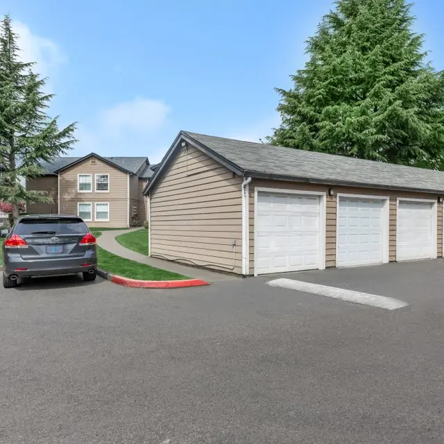 A parking area with a parked gray vehicle and storage garages in an apartment complex setting.