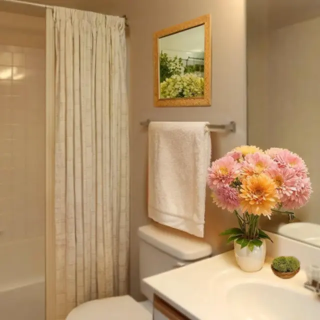 A bright and inviting bathroom featuring a large mirror, white towel on a rack, and a vibrant bouquet of flowers on the countertop.
