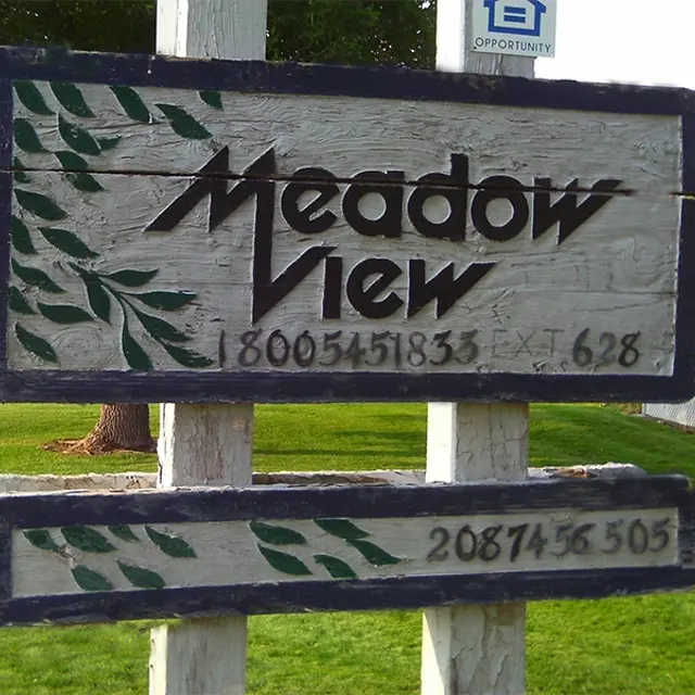 Meadow View Sign A wooden sign displaying the text 'Meadow View' with a green leaf design, and phone numbers listed below it. The sign is set against a grassy background.