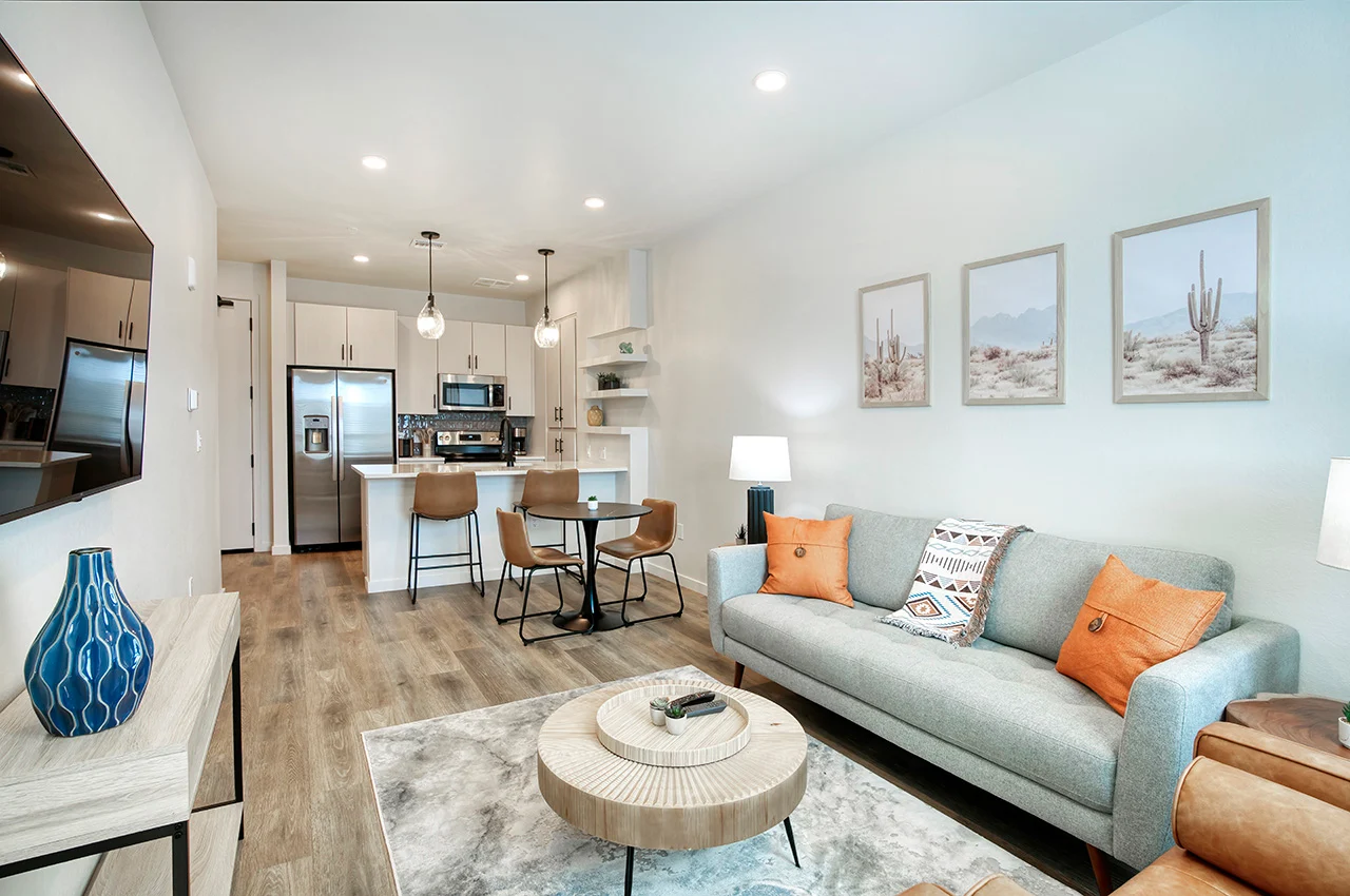Modern living room with a gray sofa, wooden coffee table, dining area, and kitchen in a bright, stylish apartment.