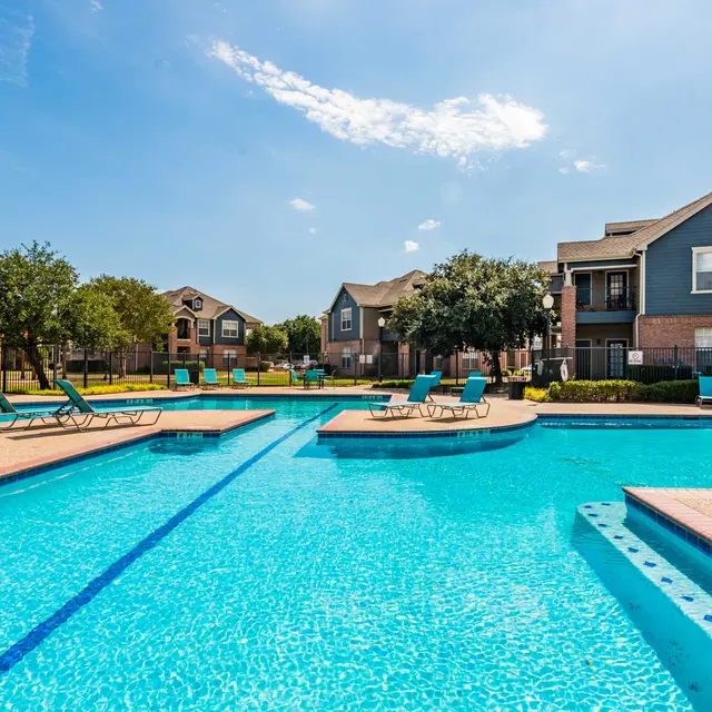 A swimming pool area surrounded by residential buildings, featuring clear blue water and lounge chairs on the pool deck.