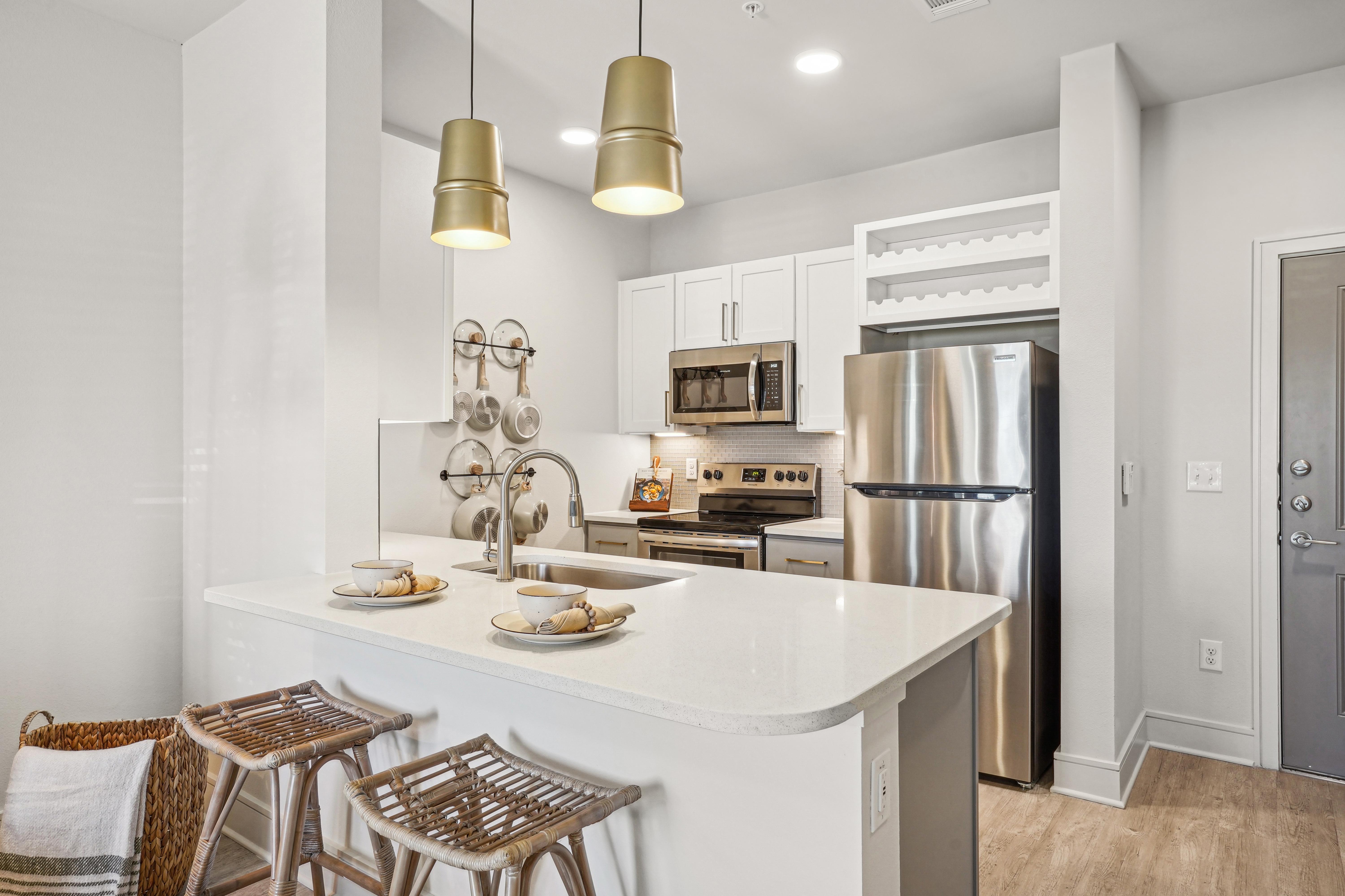 A modern kitchen featuring white cabinetry, stainless steel appliances, and a large island with bar stools.