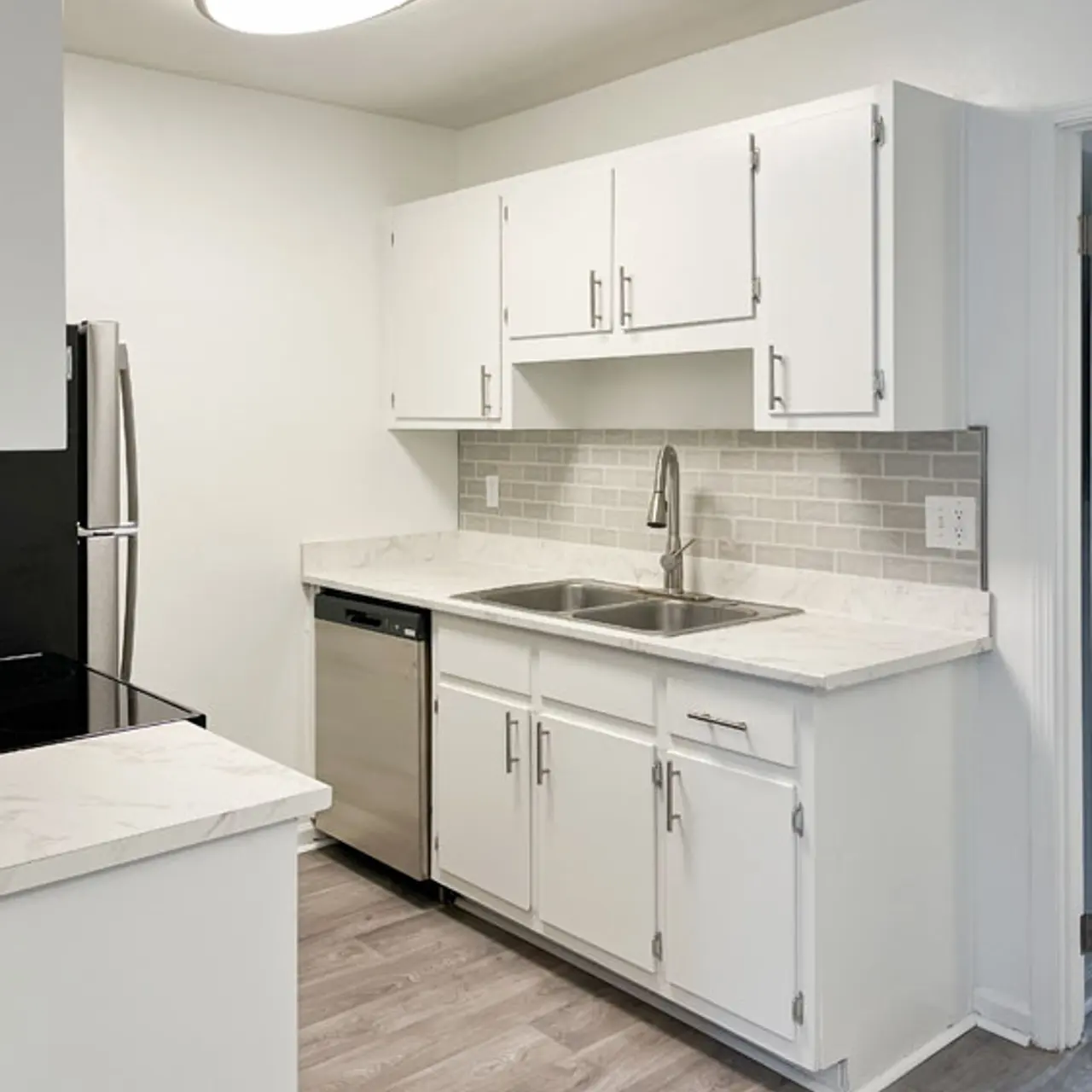 A modern kitchen featuring white cabinetry, stainless steel appliances, and a light gray backsplash with a large overhead light fixture.