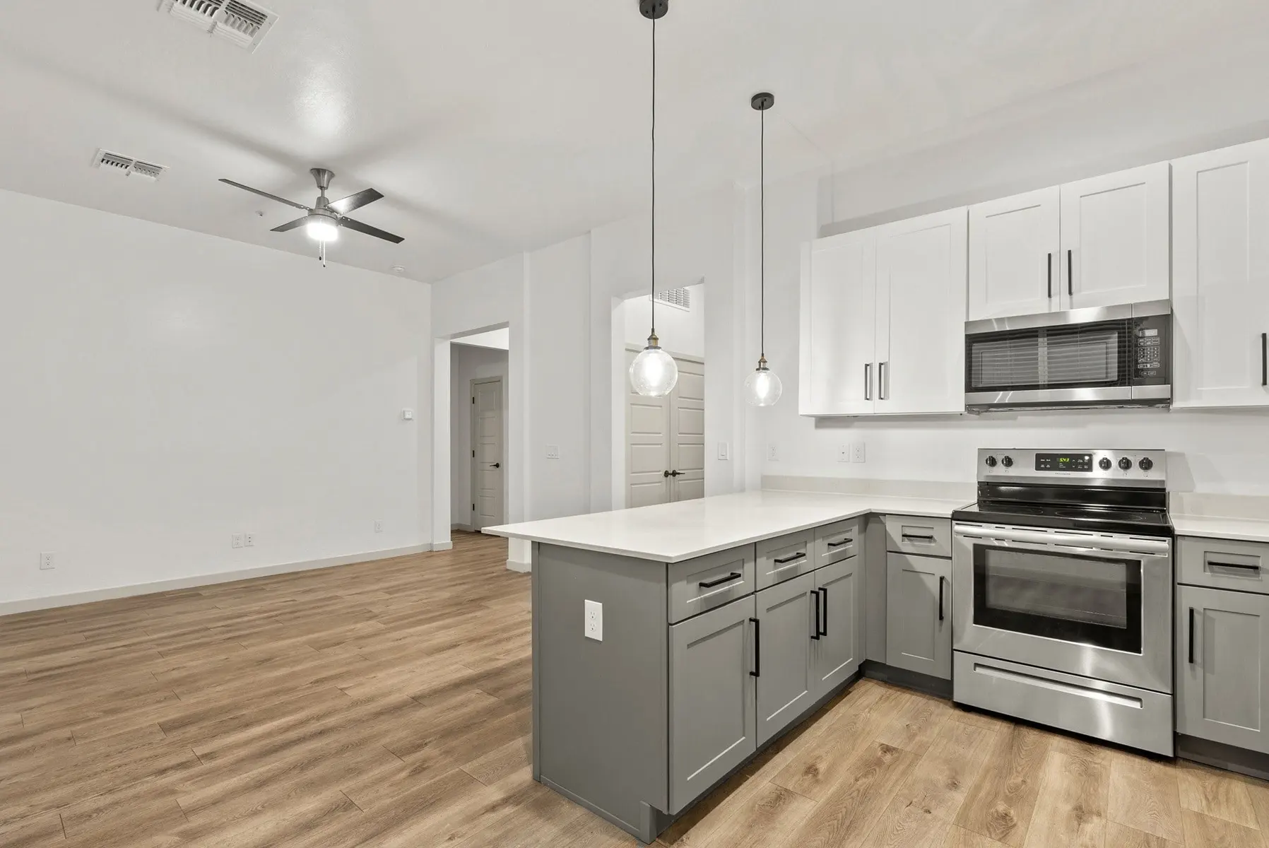 Modern kitchen with grey cabinets, stainless steel appliances, and a white countertop; open layout with wooden flooring.
