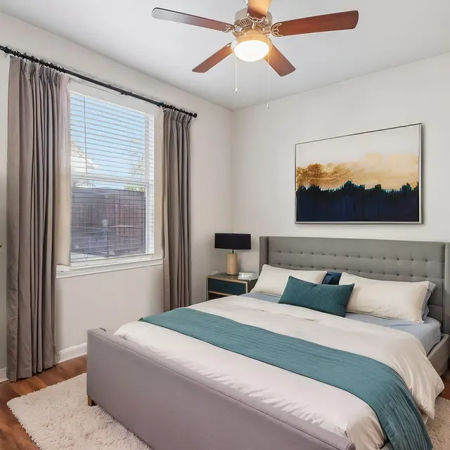 Bedroom (Staged) - Costa Almadena A cozy modern bedroom featuring a bed with a gray upholstered headboard, decorative pillows, two bedside lamps, and a decorative plant in a white pot.