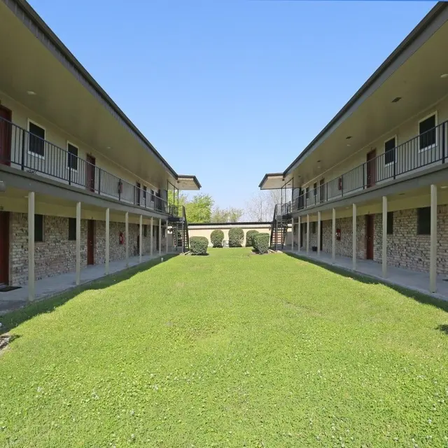 View of a courtyard in an apartment complex with two buildings facing each other, surrounded by green grass and bushes.