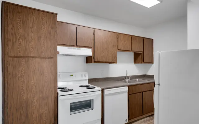 A modern kitchen featuring wooden cabinets, a white stove, a dishwasher, and a sink.