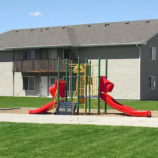 Playground Connected to Apartment Complex A playground with red slides and climbing structure in front of a two-story apartment building.