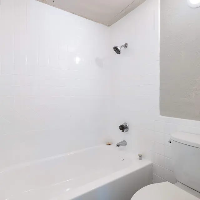A clean, minimalist bathroom featuring a bathtub, toilet, and shower fixtures on white tiled walls.