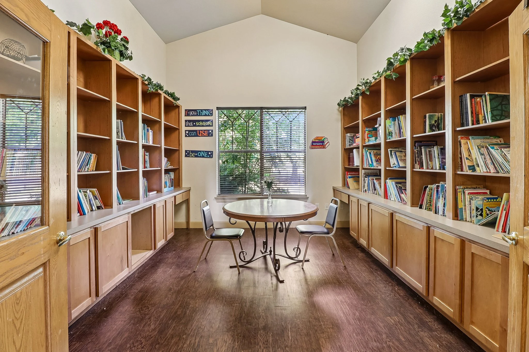 A cozy reading area with bookshelves filled with books, a round table in the center, and large windows letting in natural light.