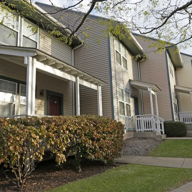 View of several townhouses with porches and landscaped shrubs in front, along a walkway.