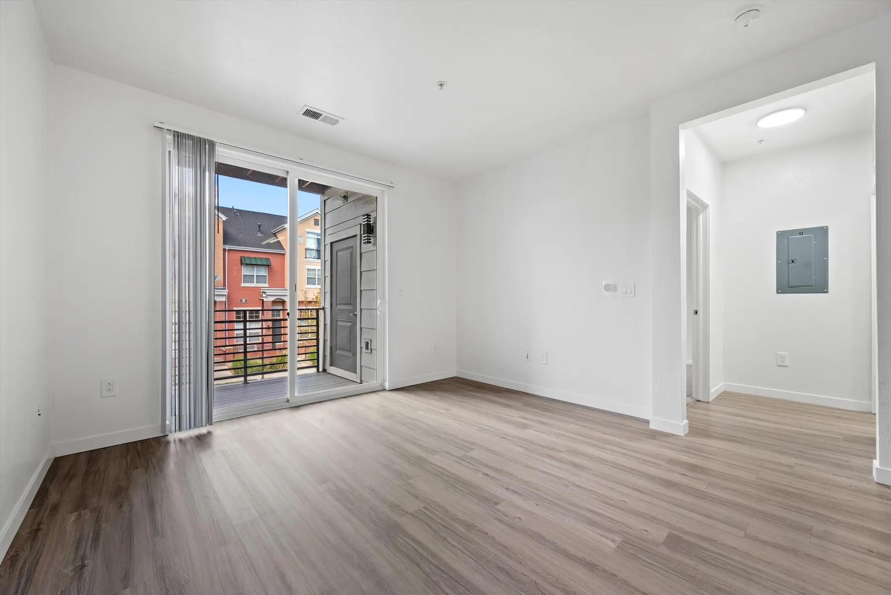 An empty living room in an apartment with sliding glass doors leading to a balcony.