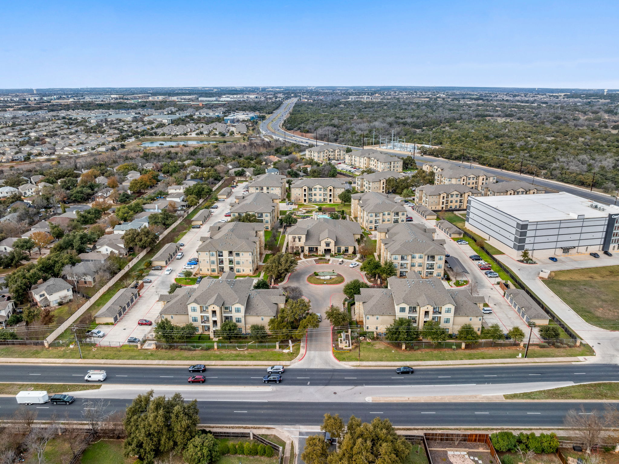 Aerial view of a multi-unit apartment complex with several buildings, surrounded by greenery and roadways.
