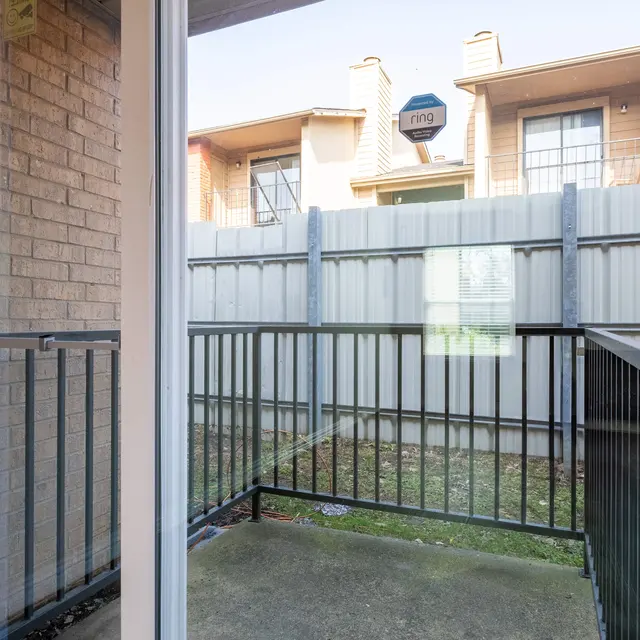 View from a balcony showing a fenced area with grass and a building in the background.