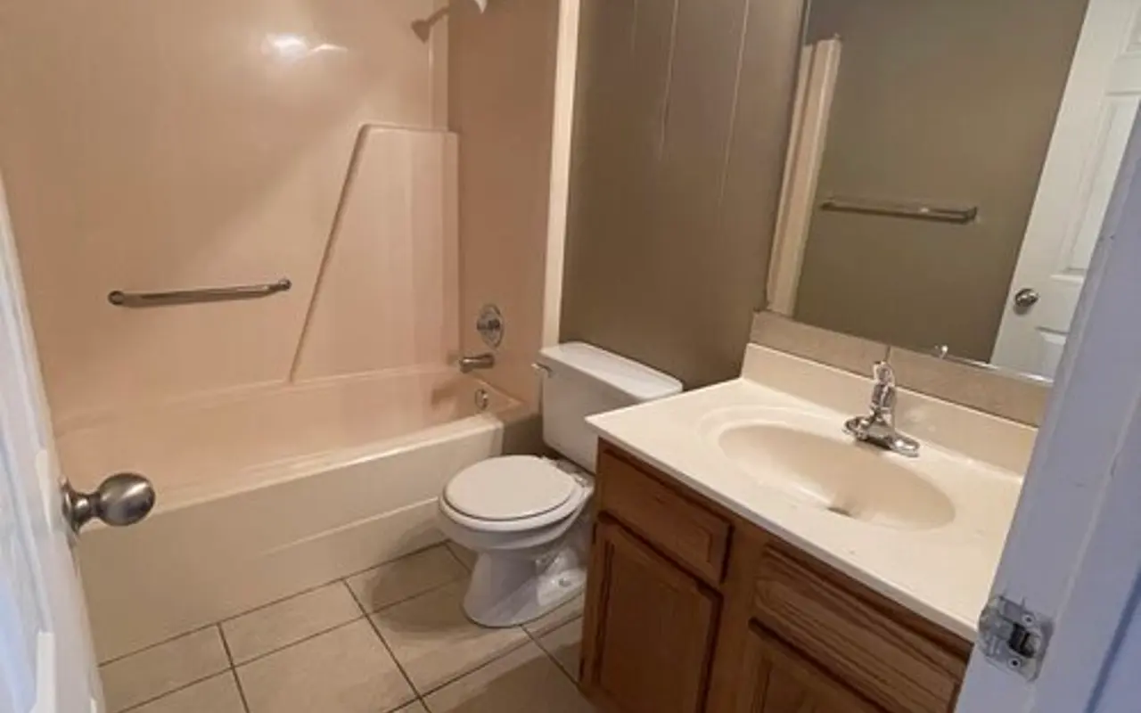 Compact Bathroom Interior A small bathroom with a bathtub, toilet, and single sink vanity. The walls are painted in a light color, and there is a large mirror above the sink.