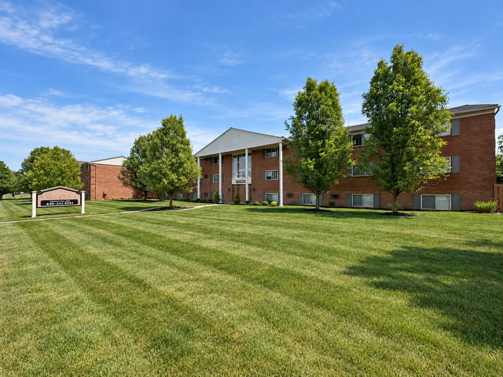 Exterior view of a brick apartment building surrounded by greenery and lawn.