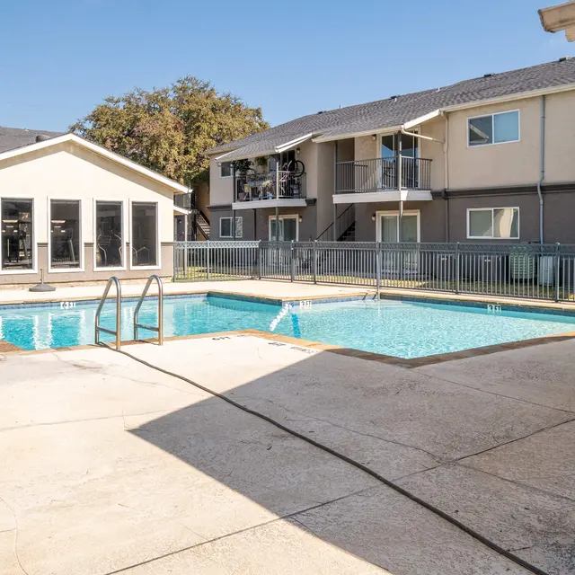 A view of a pool area surrounded by an apartment complex. The pool is clear and invites swimming, with lounge chairs nearby.