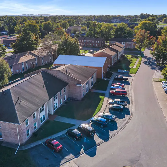 Aerial view of an apartment complex consisting of several two-story buildings, surrounded by trees and parked cars along a circular drive.