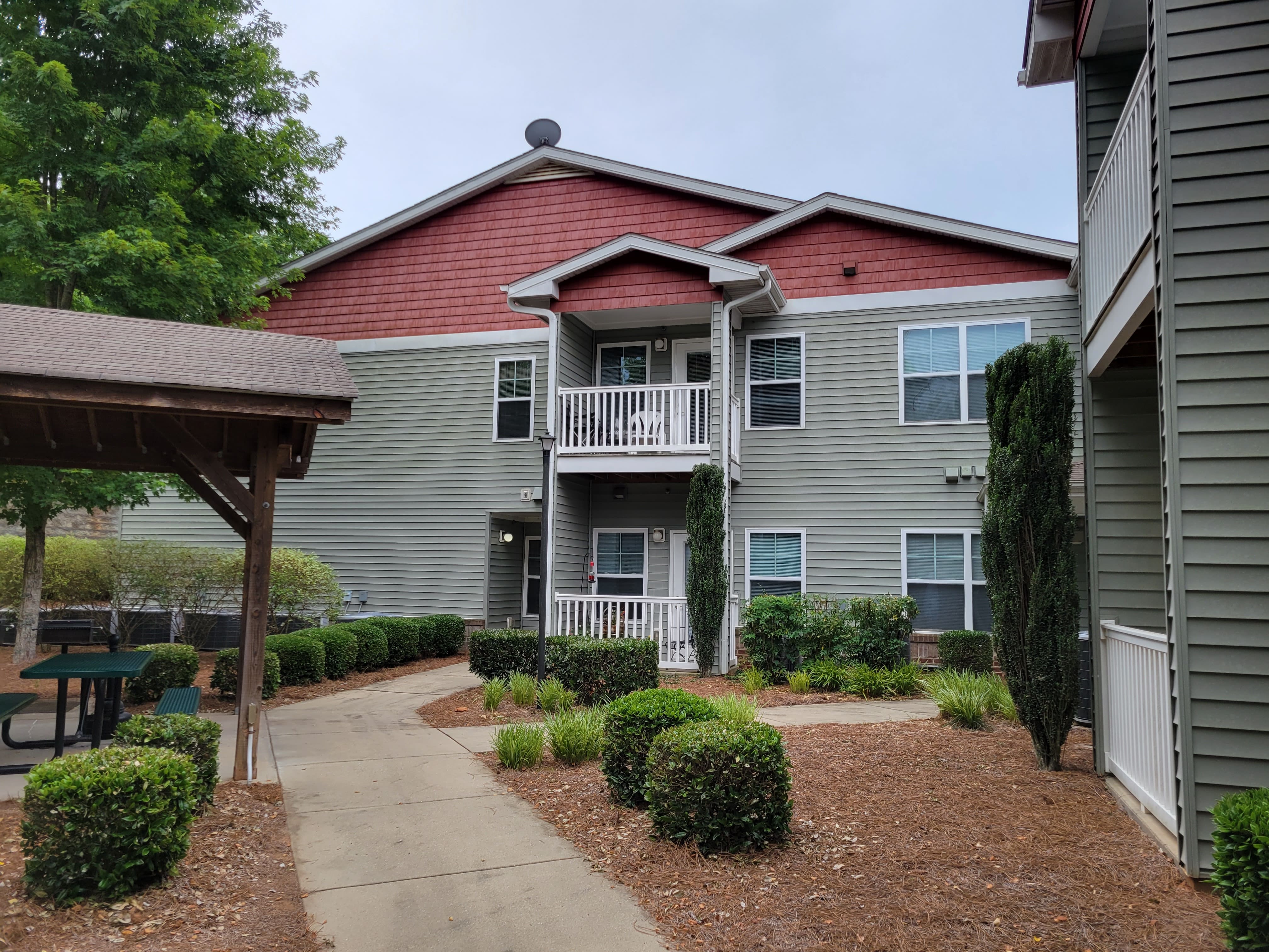 Residential Apartment Complex View of a multi-story apartment building with red and gray siding, surrounded by neatly landscaped greenery and pathways.