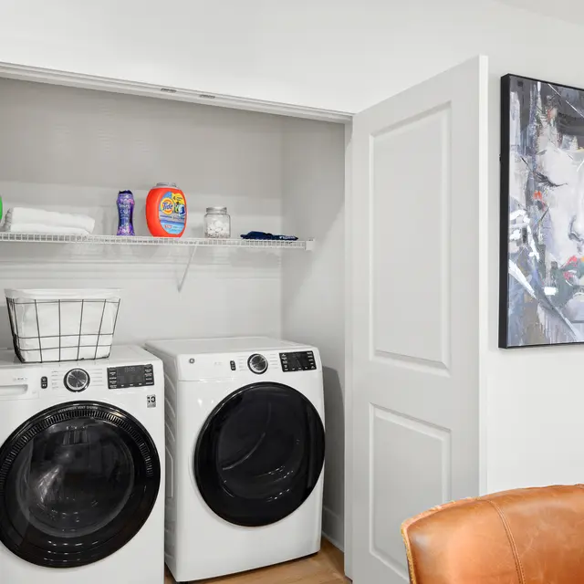 Modern laundry room with front-loading washers and a shelf containing laundry supplies
