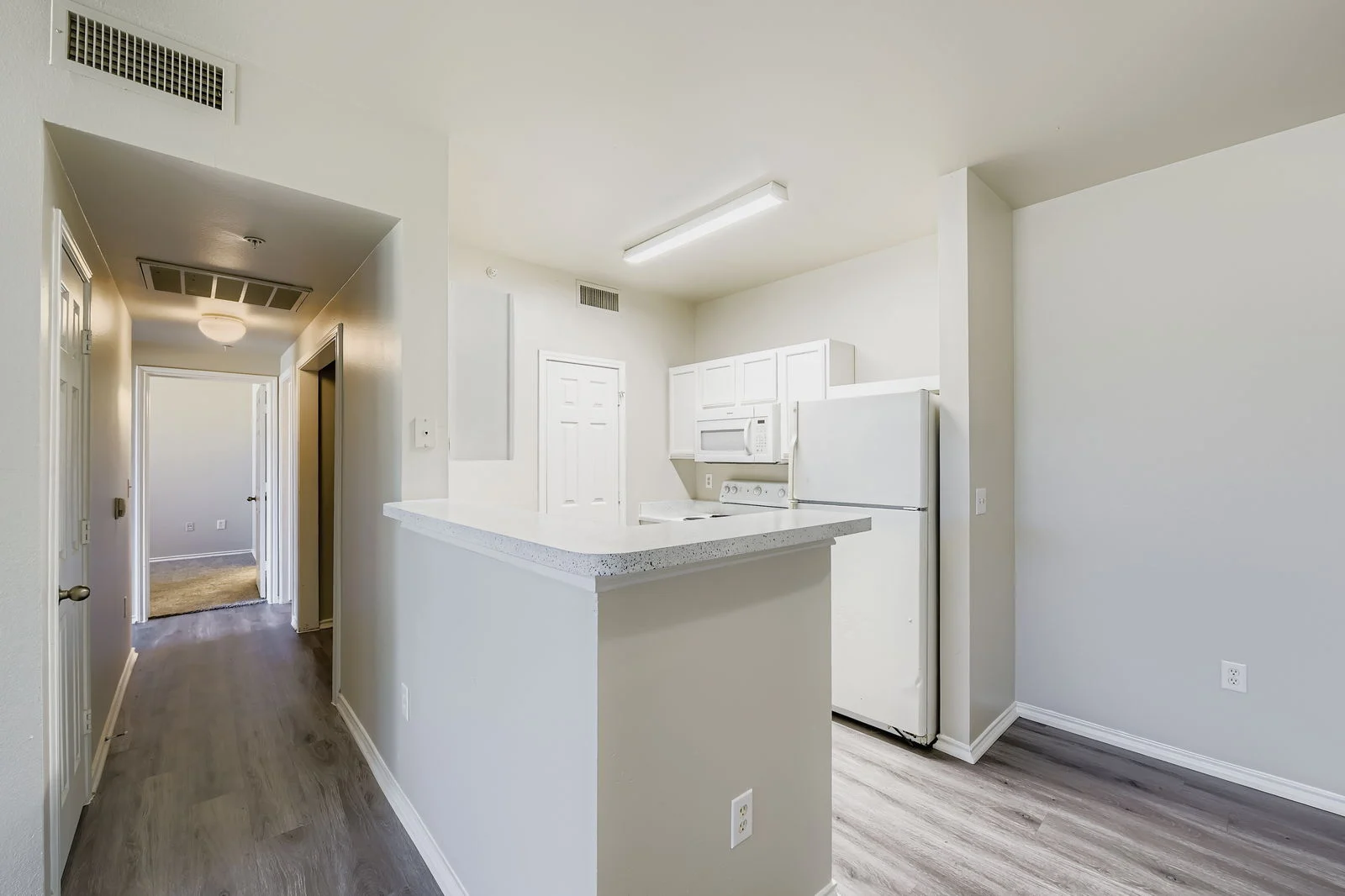 Modern Apartment Kitchen Interior view of a modern kitchen in an apartment, featuring white cabinetry, a refrigerator, and an open layout connected to a hallway.